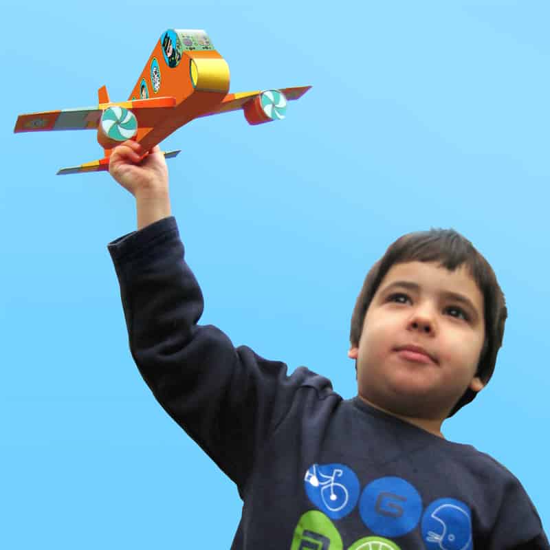 ילד חמוד משחק עם מטוס נייר, שמורכב מתוך חוברת כלי תחבורה
