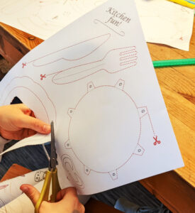 a kid cutting out parts from the preschool worksheets kitchen kit